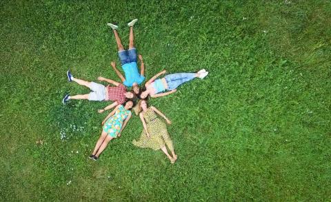 Lifestyle: Group portrait of young adults laying in grass in star formation