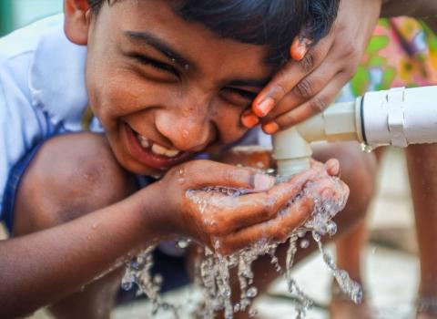 Travel: Indian boy being laughing while drinking water from a fauset in the ancient town of Hampi in India.